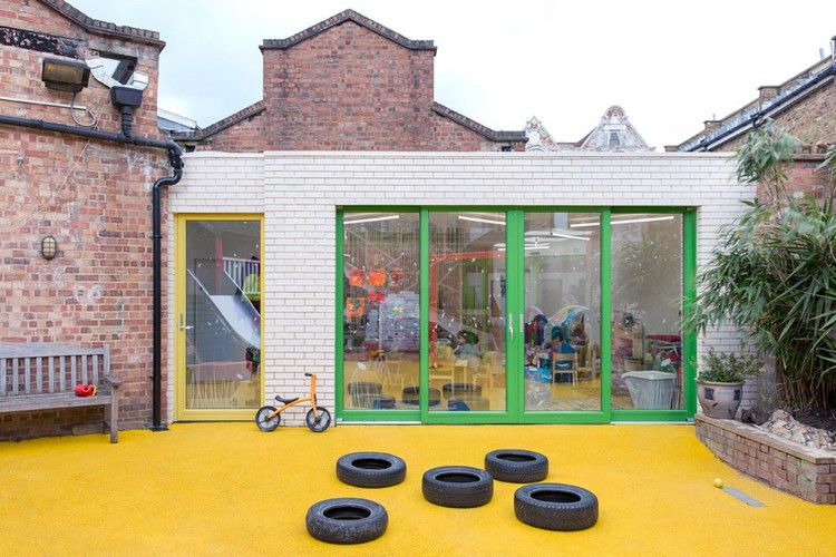 kindergarten-architektur-weiße-ziegelwand-glasschiebetüren-grün-gelber-bodenbelag-autoreifen