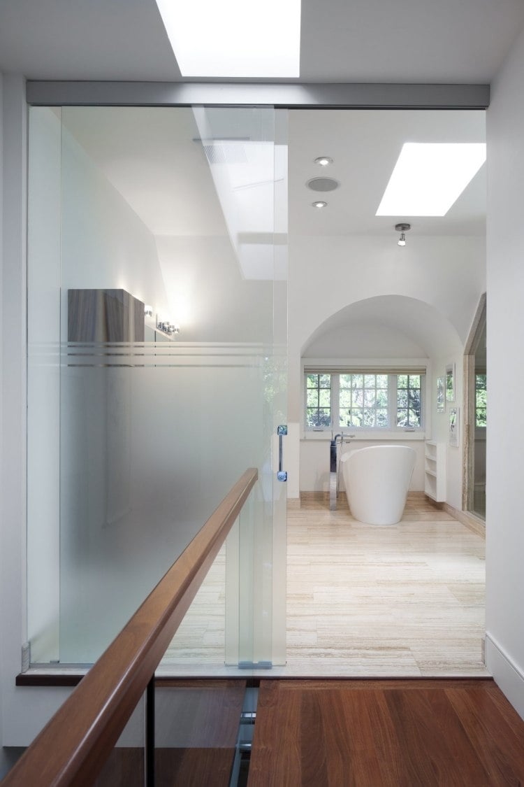 minimalistischem-design-badezimmer-glaswand-freistehende-badewanne-weiss-holz-travertinboden-handlauf