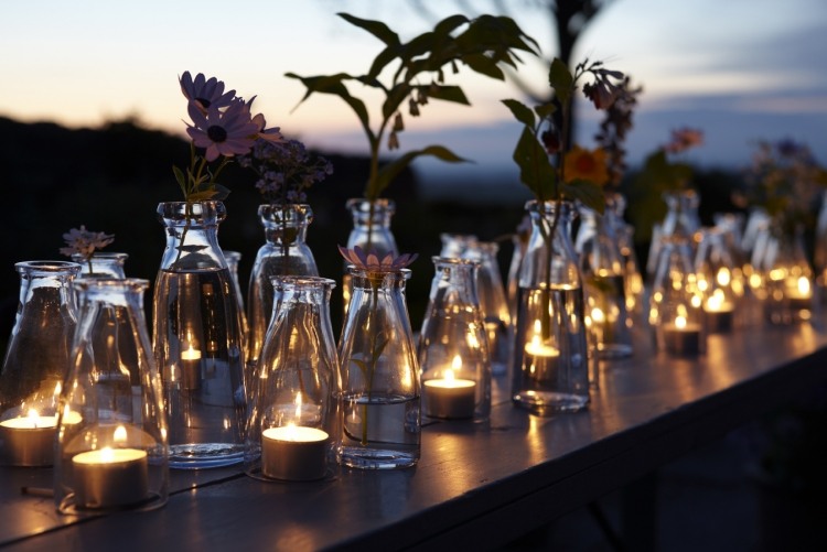 Windlicht im Garten -teelichter-glaeser-flaschen-durchsichtig-romantik-tisch-blumen