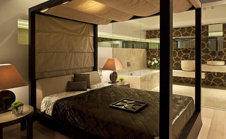 badewanne-schlafzimmer-glasbox-dunkel-braunes-bett-beige-fliesen-spiegeln