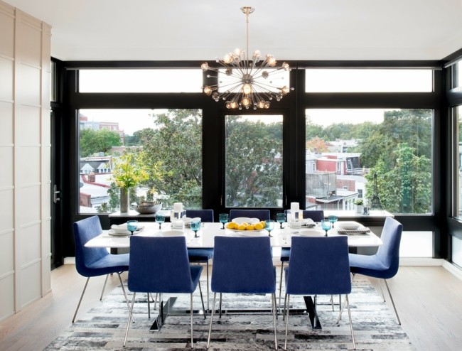  moderner Kronleuchter blaue Stühle Glaswand Teppich