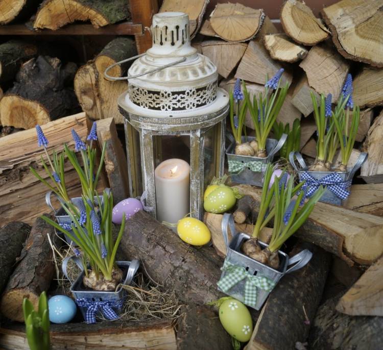 Brennholz dekorieren mit bunten Eiern und Kerze in einer Vintage-Laterne