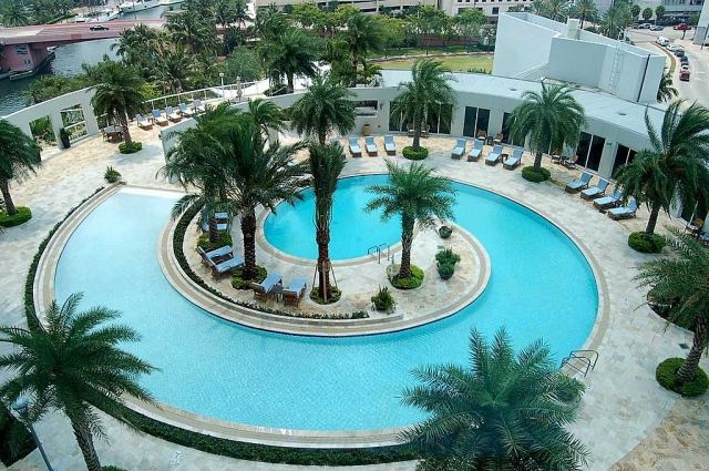 Großer-Pool-Design-mit-Insel-Palmen-Sonnenliegen-Schneckenwelle-Form