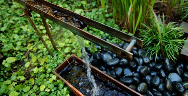 Gartenbrunnen Wasserspiele Flusssteine niedrige Vegetation