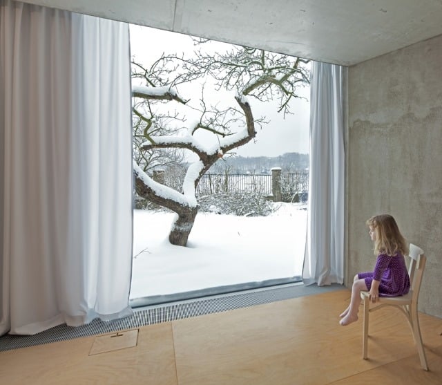 minimalistisches-haus-angepasst-an-Natur-Holz-Fußboden-raumhohe-verglasung-raue-betonwände