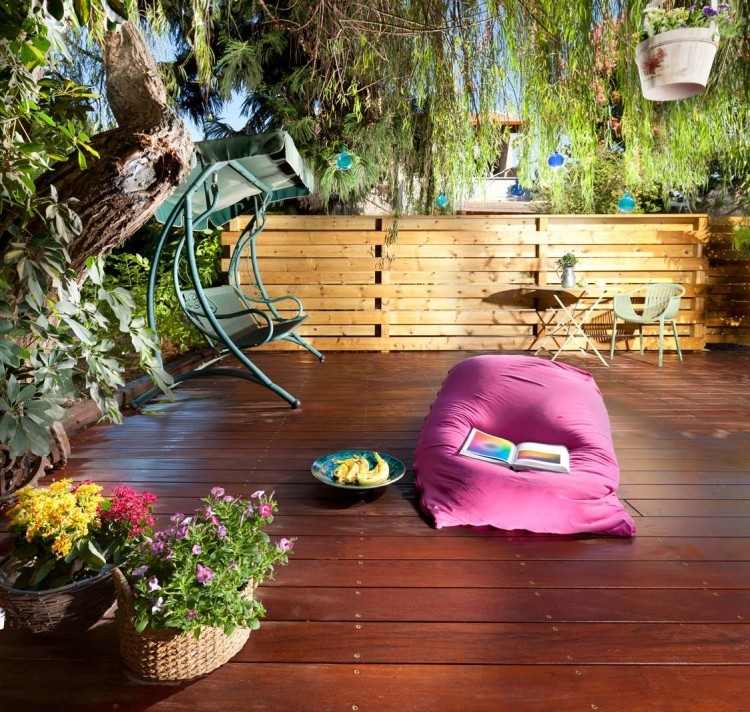 Terrasse einrichten -gestaltung-weide-sitzkissen-pink-farbenfroh-holzdiele-sichtschutz-holz-blumen