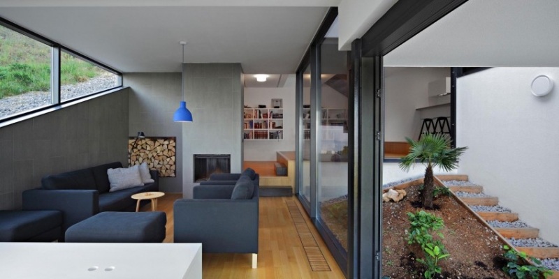 einrichtung-wohnzimmer-garten-fensterwand-kaminofen-holz-couches-schwarz-wandfarbe-grau-leuchte-ultramarin