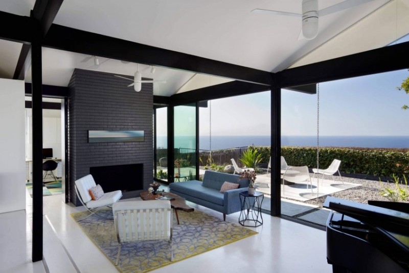 einrichtung-wohnzimmer-schwarz-weiss-teppich-pastell-violett-gelb-ziegelwand-anthrazit-terrassenfenster-meeresblick
