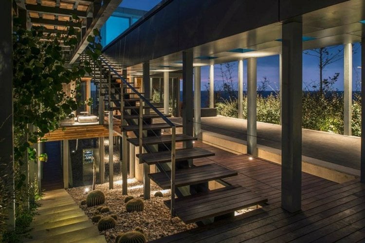 stil mediterran strandhaus treppe holz kieselsteine pflanze glasfront stahltraeger