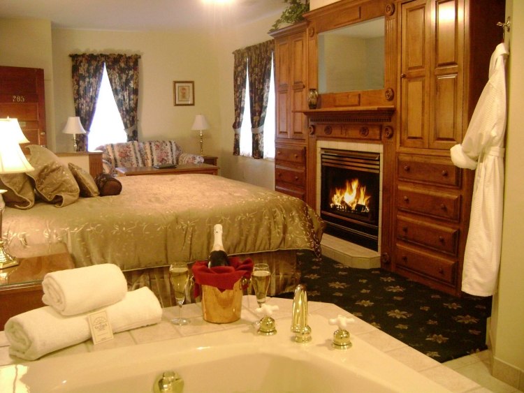 schlafzimmer-whirlpool-bett-kaminofen-holzwand-luxus-bettdecke-gold-sekt-hotelzimmer-romantisch