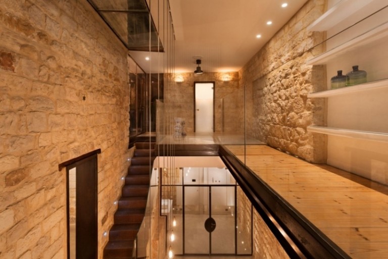 natursteinwand-innen-aussen-mauerwerk-etagen-glasgelaender-regale-beleuchtung-treppe