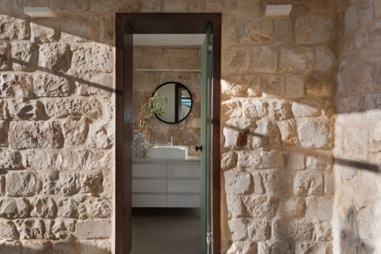 natursteinwand-innen-aussen-mauerwerk-tuer-runder-spiegel-waschbecken-weiss-untertisch-schubladen