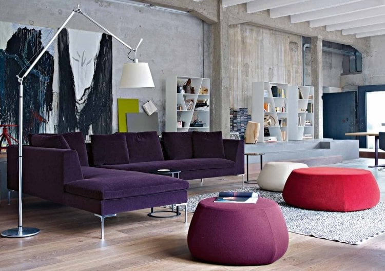 Wohnzimmer in Grau -eckcouch-betonwaende-rau-violett-poufs-hocker-nebentische