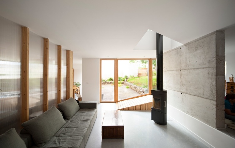 wohnzimmer-weiss-betonwand-kaminofen-couch-polster-grau-offene-decke