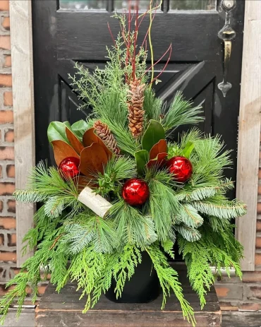 weihnachtsgesteck mit immergrünnen zweigen und roten weihnachtskugeln