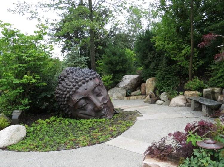 asiatische-gartendeko-buddha-statue-metall-sitzbank-stein-gruen-baeume-garden-findling