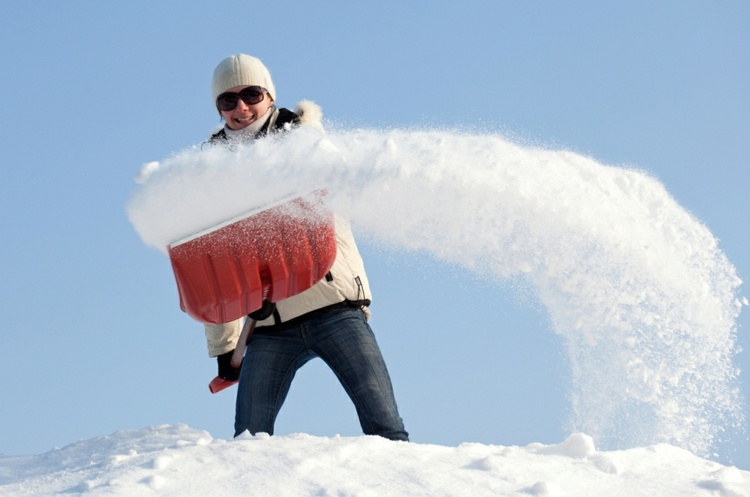 winterdienst-schneeräumen-frau-lächeln-winterbekleidung-kalt-jacke-mütze-weiß-jeans-schneeschaufel.jpg