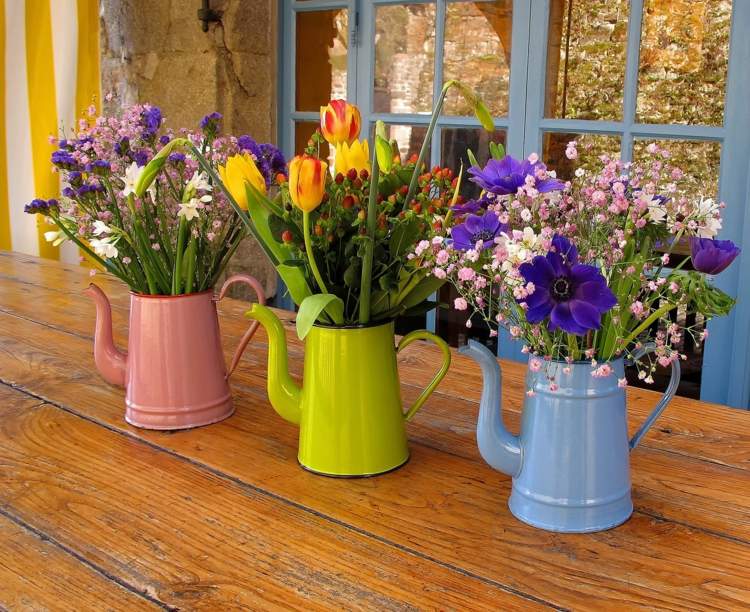 Frühlingsblumen als Sträuße in bunten Kannen aus Metall statt in Vasen