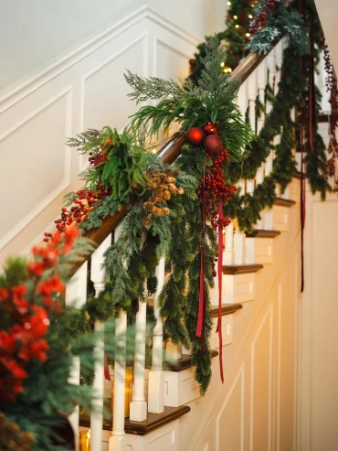 treppengeländer mit immergrünen zweigen, beeren, zapfen und warmen kerzenlichtern