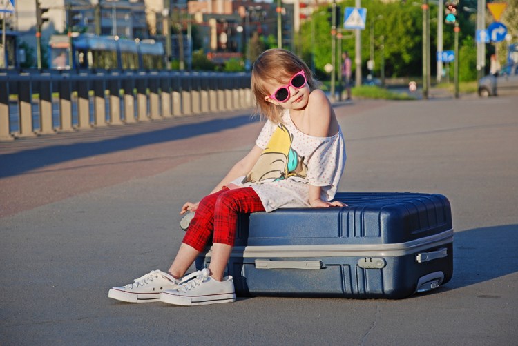 Urlaub mit Kindern Mädchen auf Koffer sitzend was man beachten sollte