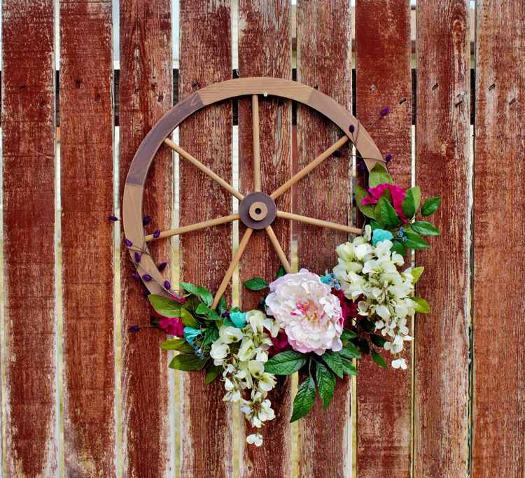 Wagenrad aus Holz mit Kunstblumen dekorieren und am Gartenzaun aufhängen