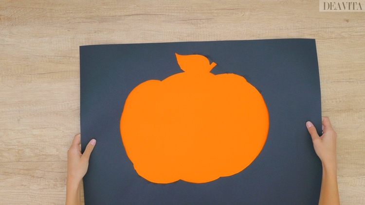 Die Kürbis Schablone auf das orange Tonpapier legen und festkleben
