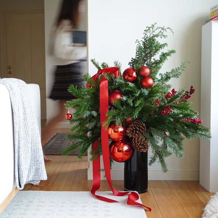arrangement aus sattem tannengrün glänzenden roten kugeln und langen satinbändern schwarze vase