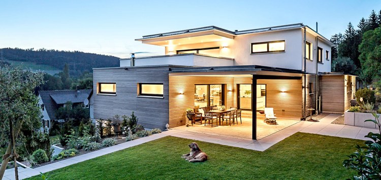 modernes Holz Fertighaus mit überdachter Terrasse Rasenfläche Außenbeleuchtung