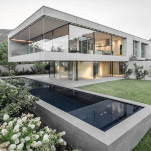 sichtbeton haus casa mf große glasfenster modernes minimalistisches design vorderansicht rasen schwimmbecken berg hang blüen