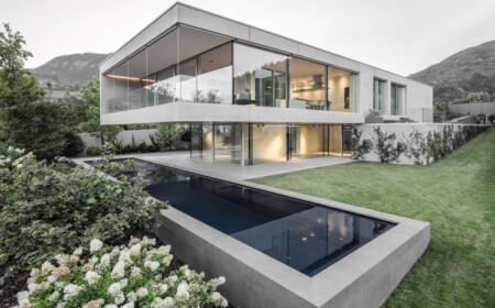 sichtbeton haus casa mf große glasfenster modernes minimalistisches design vorderansicht rasen schwimmbecken berg hang blüen