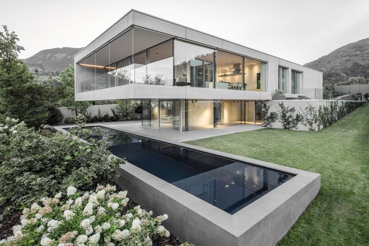 sichtbeton haus casa mf große glasfenster modernes minimalistisches design vorderansicht rasen schwimmbecken berg hang blüen