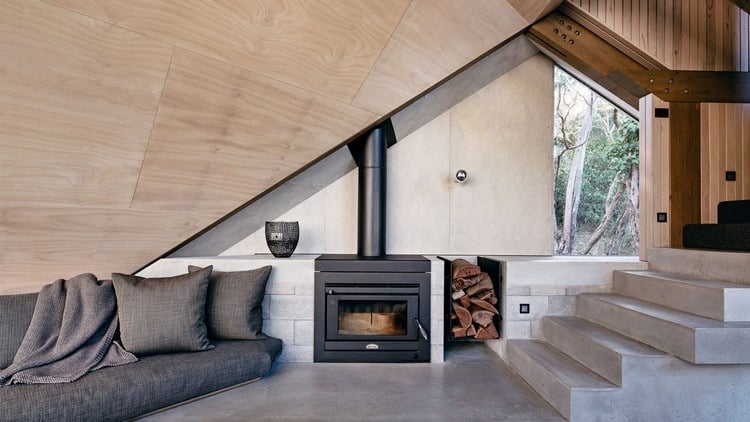 design ferienhaus schrägdach küstenwald moderne berghütte außergewöhnliche form sofa kamin beton treppe