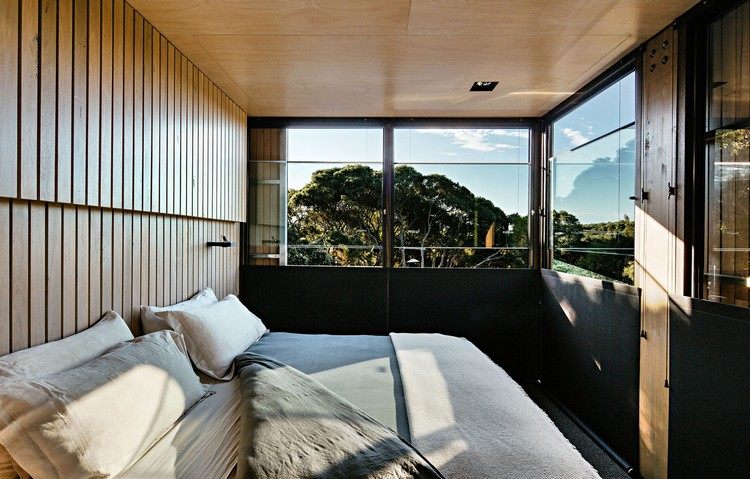 design ferienhaus schrägdach küstenwald moderne berghütte schlafzimmer bett fenster aussicht sonnenlicht