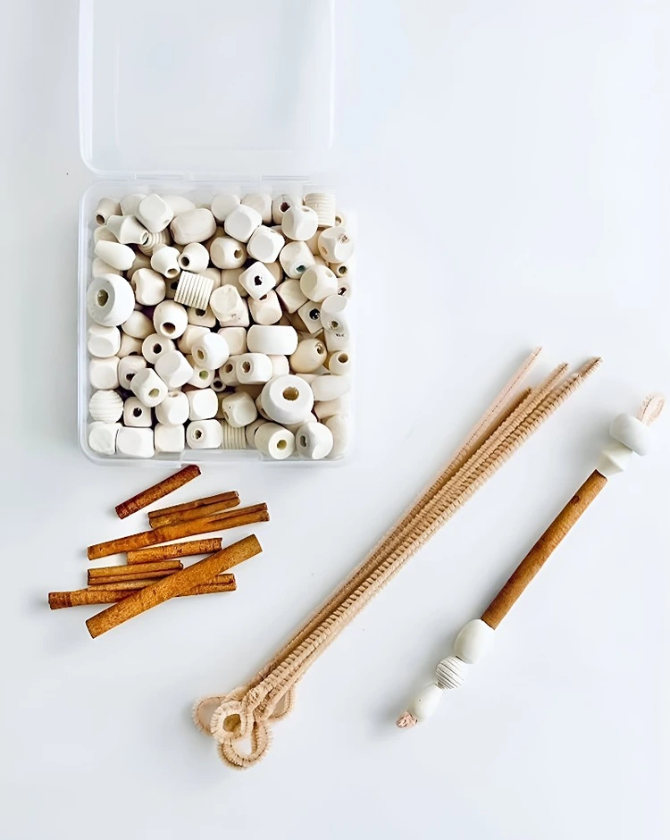 Pfeifenreiniger durch Zimtstangen und Holzperlen fädeln