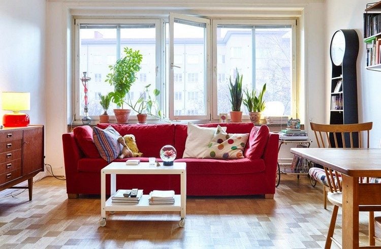 sofa vor fenster aufstellen wohnzimmer stilvoll couch rot einrichten couchtisch sofatisch rollen kissen bunt retro stil wanduhr pflanzen esstisch