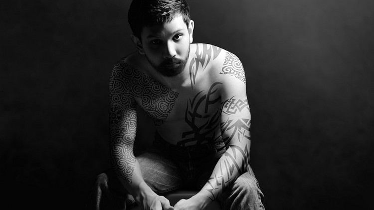 junger mann mit ganz körper tätowierungen sitzend in schwarz weiß fotografie