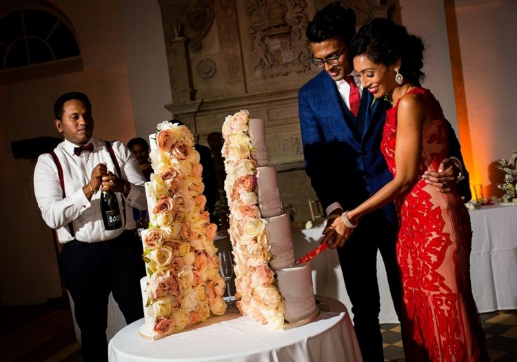 Ein Brautpaar schneidet die gespaltene Hochzeitstorte mit Blumen an