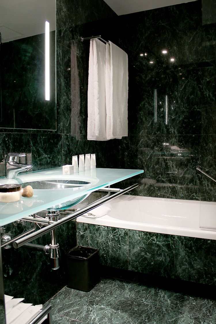 Badezimmer mit Badewanne grüne Marmorfliesen Glaswaschbecken transparent