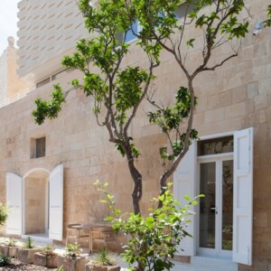 außenfassade vom renovierten kutscherhaus mit weißen türen und garten mit baum in malta