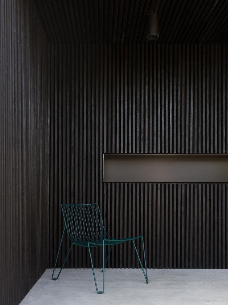 außenterrasse mit dunklen lamellen aus holz als fassadenverkleidung mit designer stuhl in blau