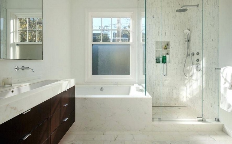 badewanne vor fenster mit duschkabine und nische im bad in weiß marmor und holz