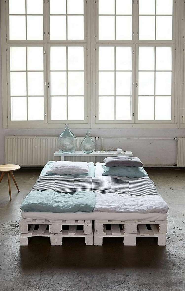 palettenbett für zwei mit matratze in großem raum mit fenstern und minimalistischem design