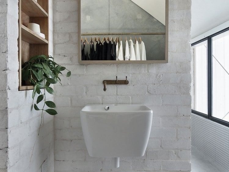waschbecken mit rustikalem wasserhahn und spiegel neben bad nische auf ziegelwand in weiß