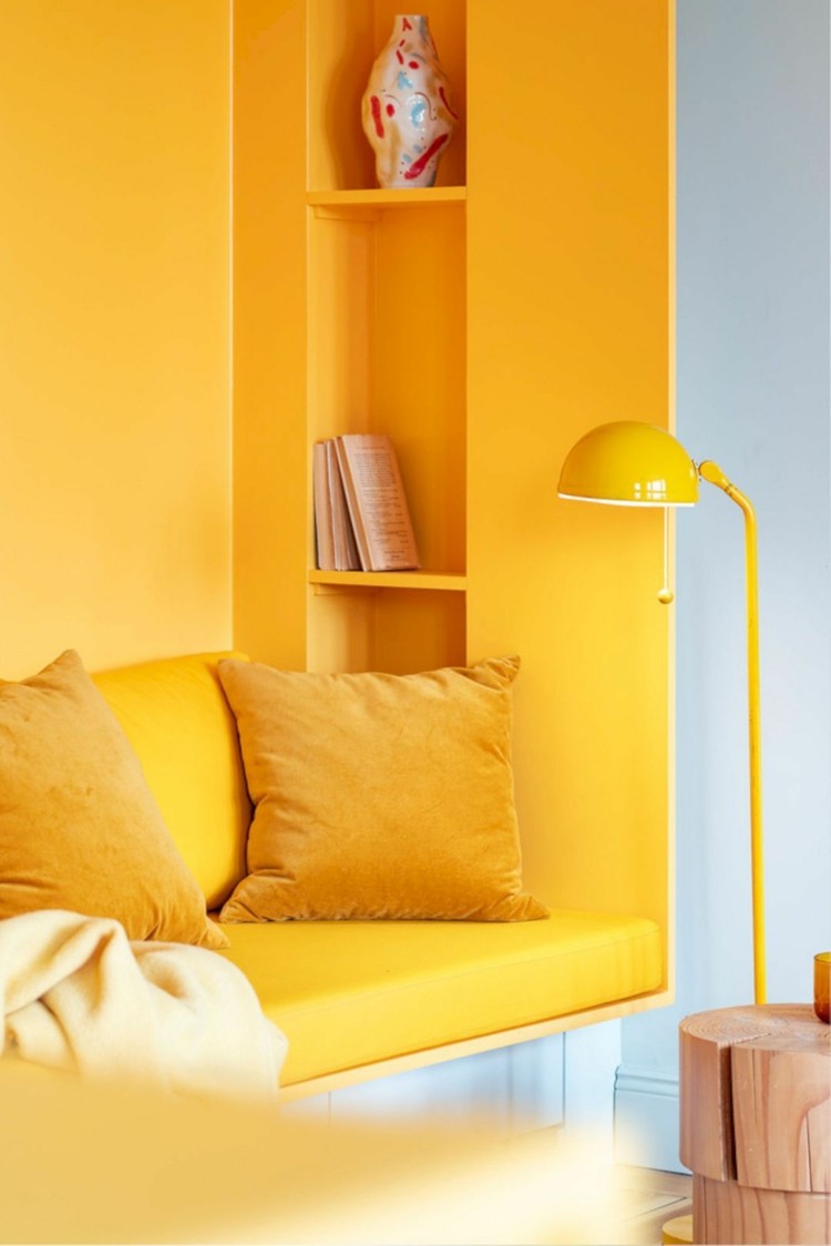 Die Farbe Gelb im Sitzbereich mit eingebautem Regal findet sich auch in den Kissen wieder