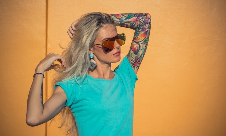 frau-mit-sonnenbrille-und-blauem-t-shirt-zeigt-ihre-arm-mit-buntem-tattoo-design