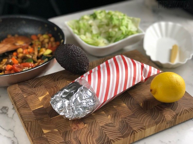 in alufolie und papiertüte eingewickelte vegetarische wrap mit eisbergsalat für unterwegs