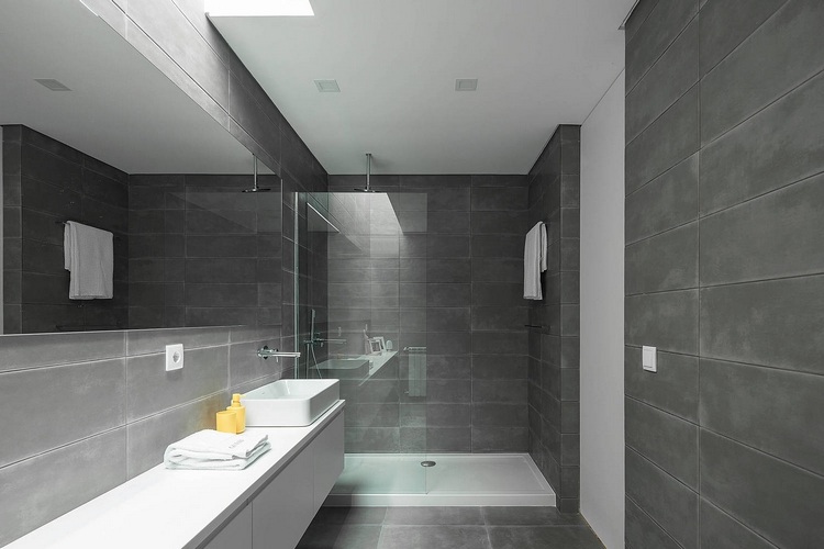 minimalistisch gestaltetes badezimmer in grau mit langem spiegel und badeschrank in weiß vor duschkabine