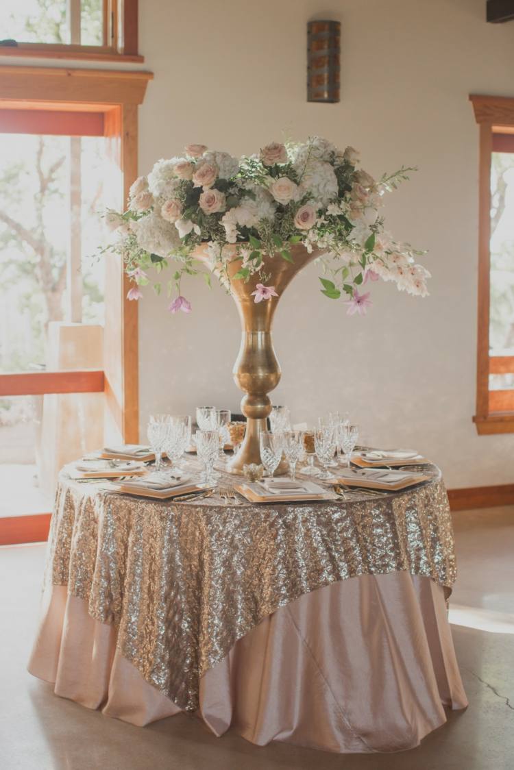 Runde Tische mit großem Blumenarrangement in der Mitte und Tischdecken in Gold und Rosa