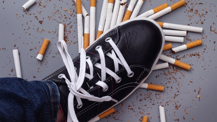 bein mit sportschuh in schwarz weiß tritt auf zerstreute zigaretten als symbol für rauchen aufhören