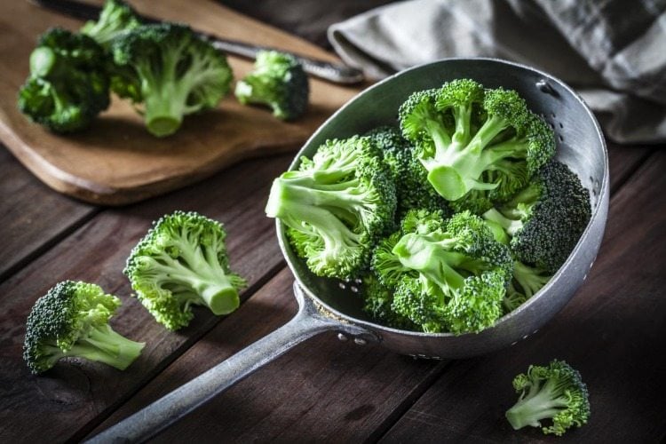 brokkoli röschen geschnitten in einer schöpfkelle auf holztisch